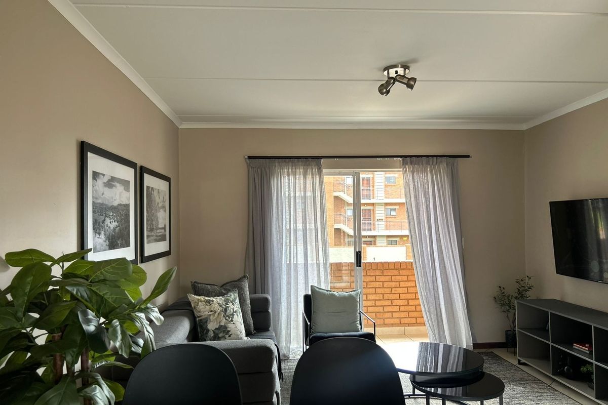 A well-maintained living room featuring a sliding glass door leading to a balcony, neutral wall tones, and modern ceiling spotlighting.
