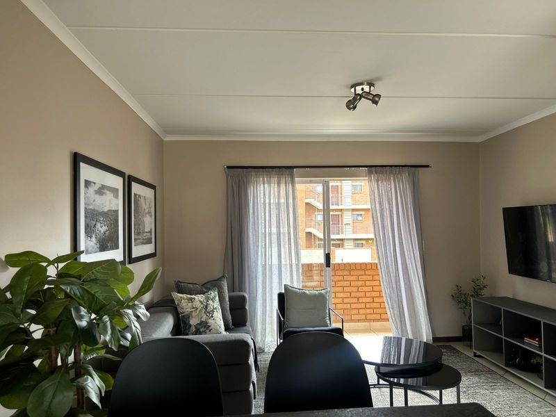 A well-maintained living room featuring a sliding glass door leading to a balcony, neutral wall tones, and modern ceiling spotlighting.
