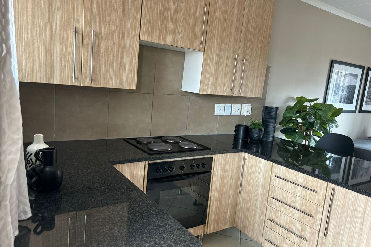 Modern kitchen featuring light wood-grain cabinetry, dark granite countertops, a built-in electric oven and hob, and neutral tiled backsplash.