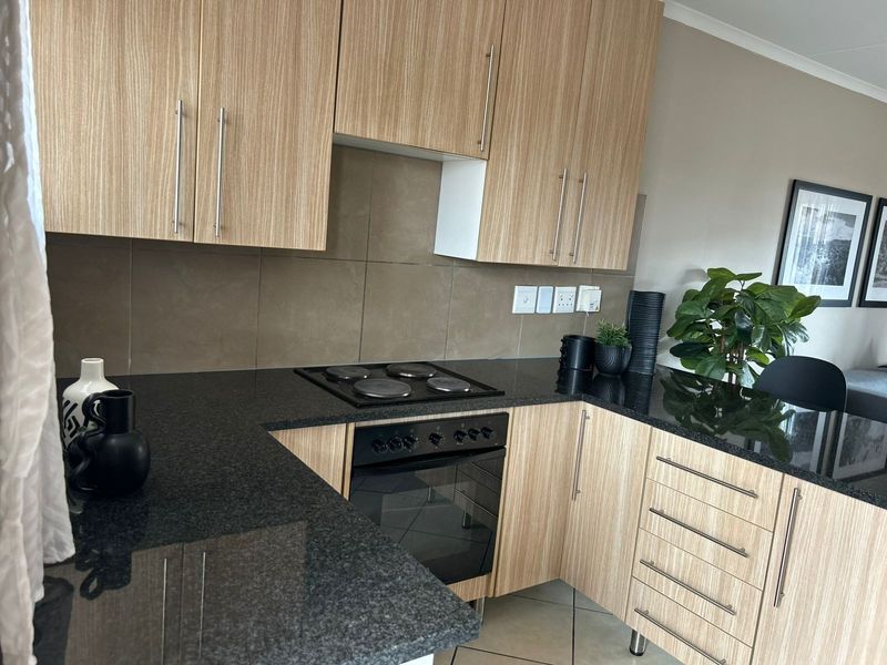 Modern kitchen featuring light wood-grain cabinetry, dark granite countertops, a built-in electric oven and hob, and neutral tiled backsplash.