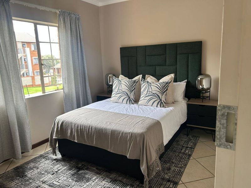 A well-maintained bedroom featuring tiled flooring and a window with security bars, offering a comfortable and functional living space.