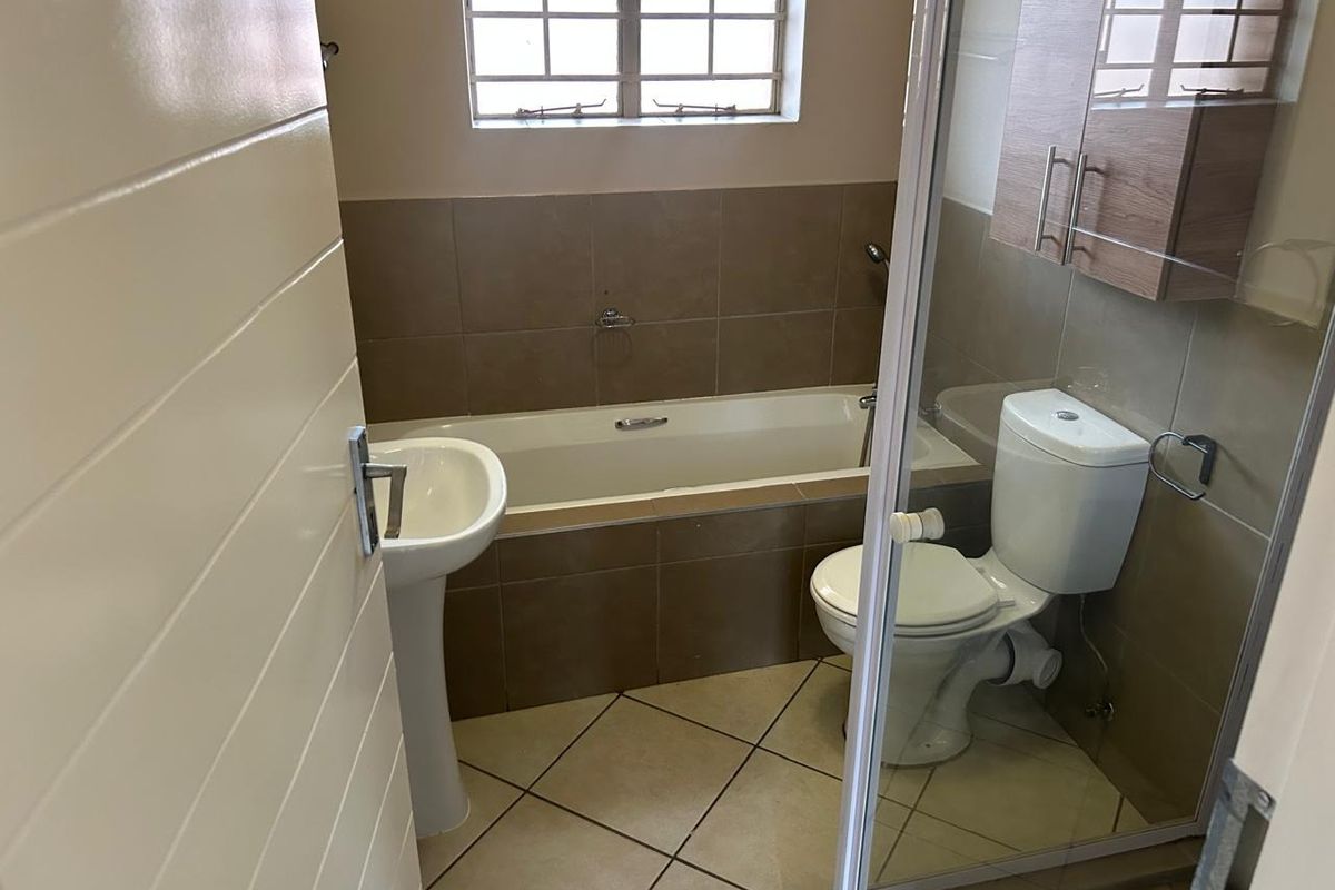 A functional bathroom featuring a pedestal basin, built-in bathtub, toilet, and wall-mounted storage cabinet with neutral tiled finishes.