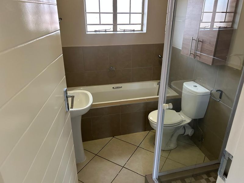 A functional bathroom featuring a pedestal basin, built-in bathtub, toilet, and wall-mounted storage cabinet with neutral tiled finishes.