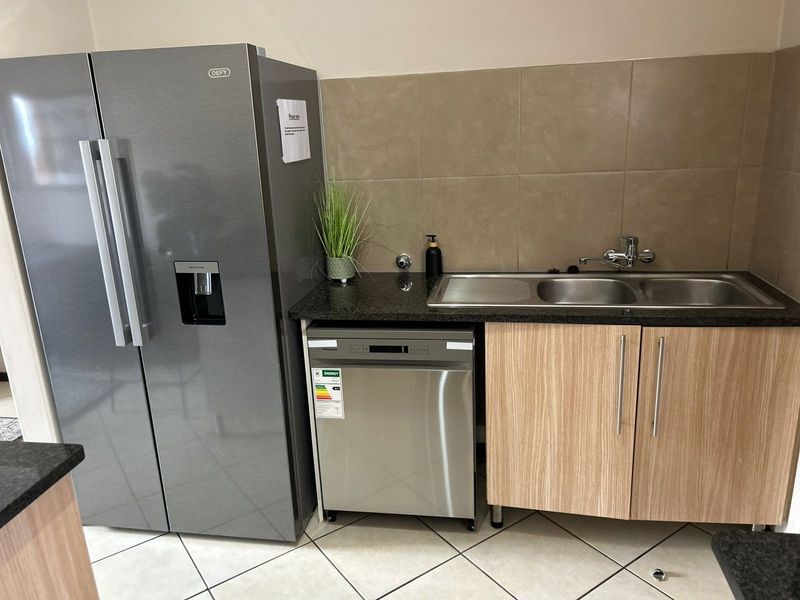 A functional kitchen area featuring granite countertops, double sink, tiled backsplash, and light wood-finish cabinetry with integrated appliance space.