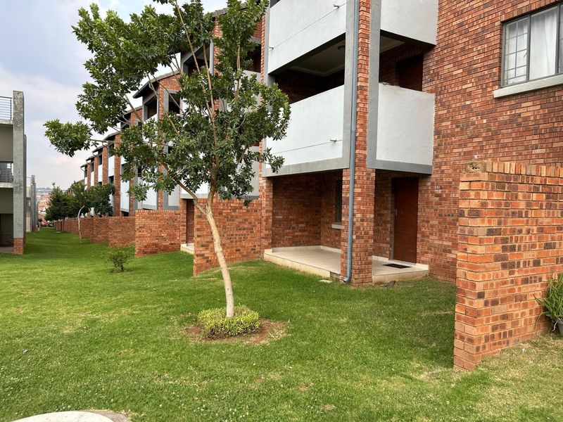 Exterior view of a multi-story face brick apartment complex featuring ground floor patios and upper-level balconies overlooking a shared lawn area.