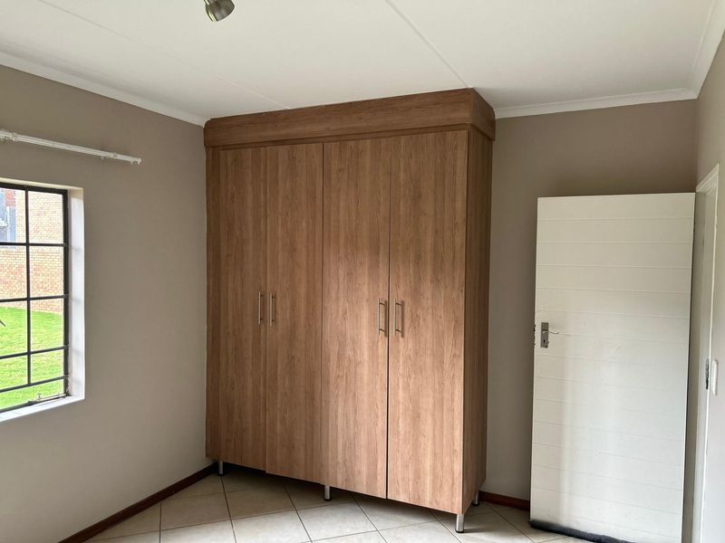 A clean, empty bedroom featuring neutral walls, tiled flooring, and a large built-in wooden wardrobe with ample storage space.