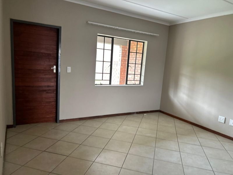 A clean, empty living room featuring neutral wall paint, tiled flooring, a timber door, and a steel-framed window.