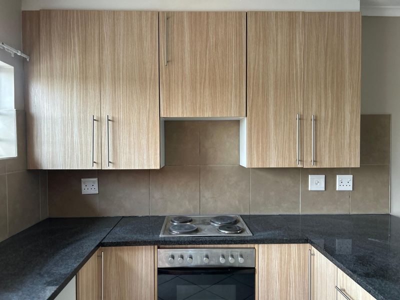 A functional kitchen featuring wood-grain cabinetry, dark granite countertops, a built-in oven, and an electric hob with a tiled backsplash.