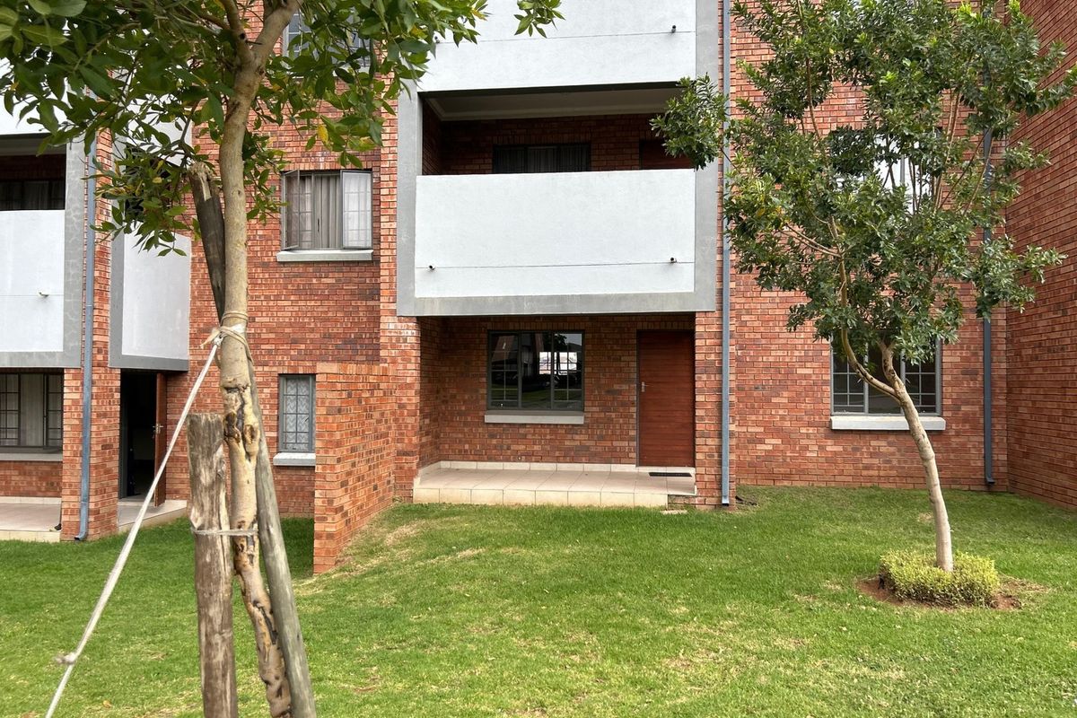 Rear view of a face brick apartment building featuring a ground floor tiled patio, landscaped garden area, and aluminium window frames.