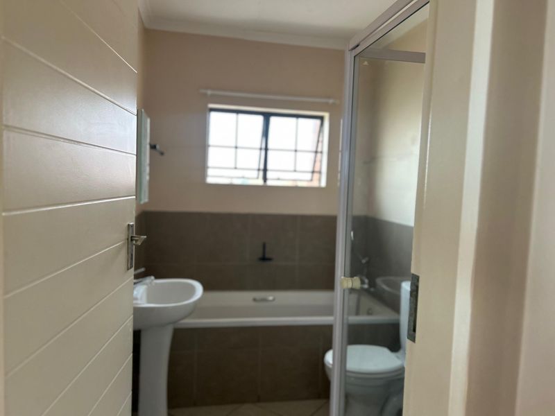 A functional bathroom featuring a pedestal basin, bathtub, and a separate shower enclosure with neutral wall tiling.