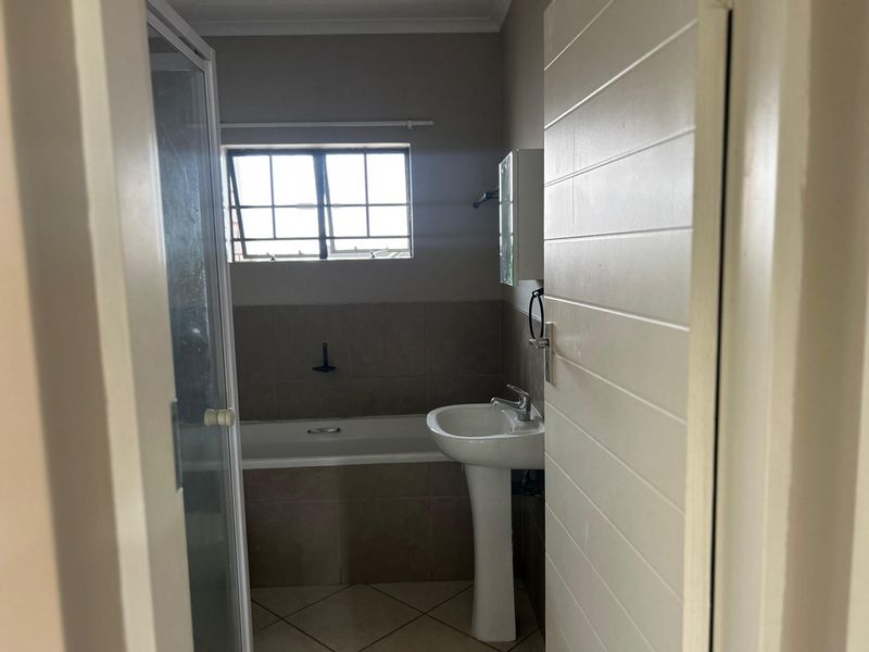 A functional bathroom featuring a pedestal basin, a bathtub, and a separate shower enclosure with neutral wall and floor tiling.