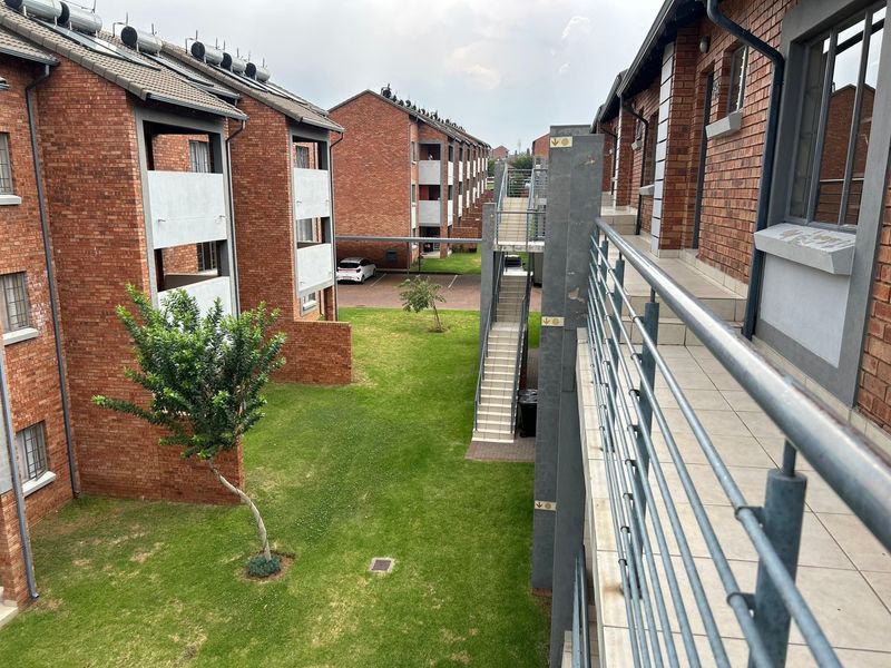 View of the apartment complex exterior featuring face brick buildings, communal garden space, external staircases, and elevated walkways with metal railings.