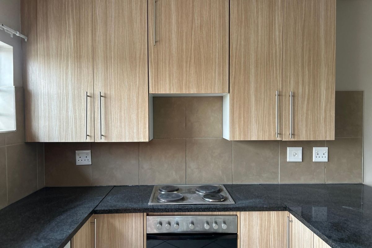 A functional kitchen featuring wood-grain cabinetry, dark granite countertops, a built-in oven, and an electric hob with a tiled backsplash.