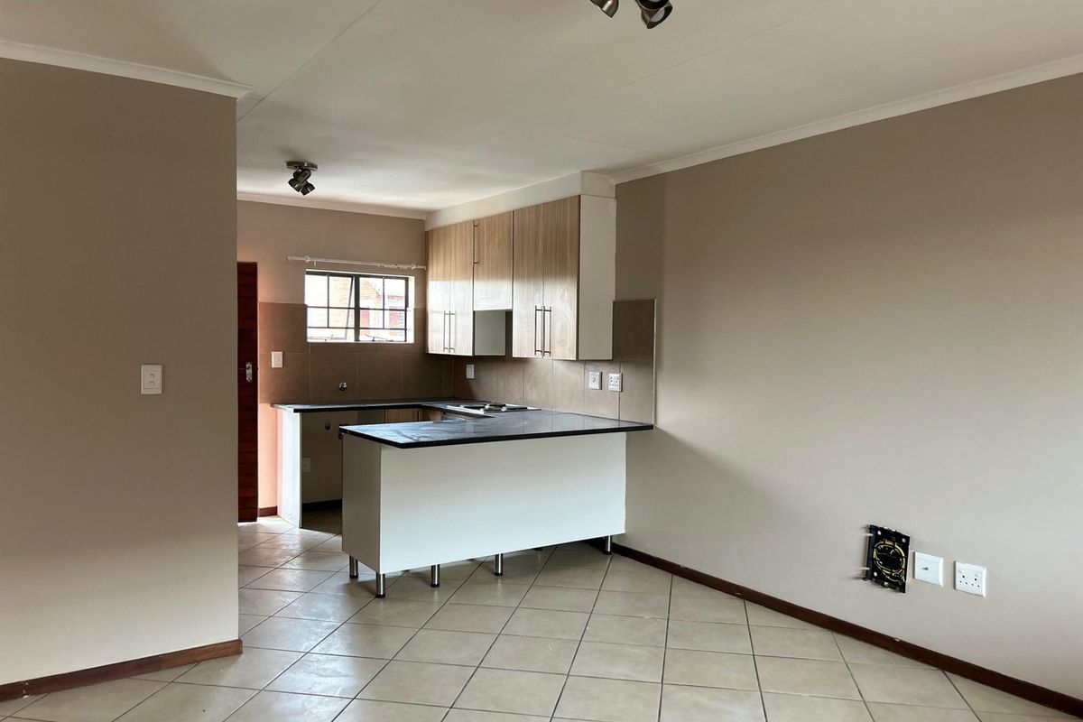 Open-plan kitchen and living area featuring tiled flooring, built-in cabinetry with laminate countertops, and integrated hob with extractor fan.