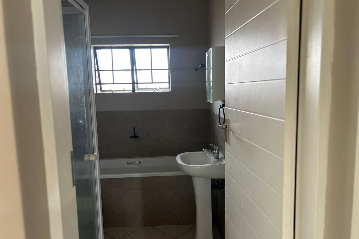 A functional bathroom featuring a pedestal basin, a bathtub, and a separate shower enclosure with neutral wall and floor tiling.