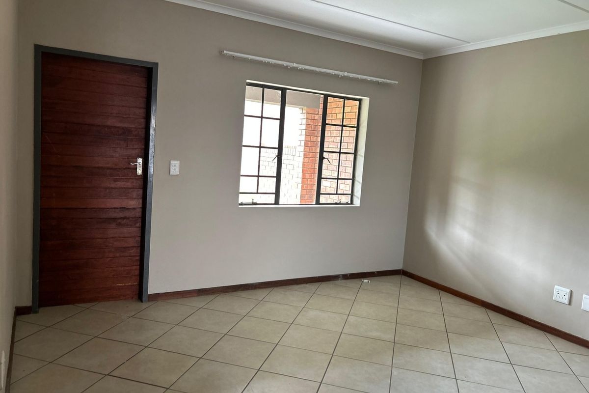 A clean, empty bedroom featuring neutral wall tones, tiled flooring, and a classic timber door, offering a versatile space ready for personalization.