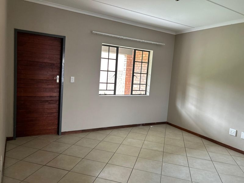 A clean, empty bedroom featuring neutral wall tones, tiled flooring, and a classic timber door, offering a versatile space ready for personalization.