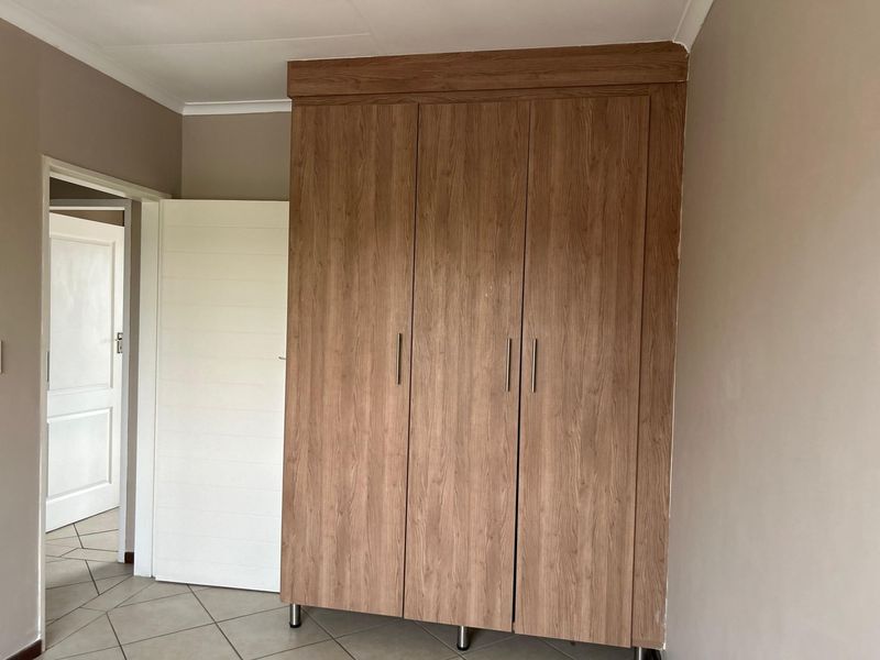 A clean bedroom featuring a modern wood-finish built-in wardrobe, neutral wall tones, and tiled flooring.