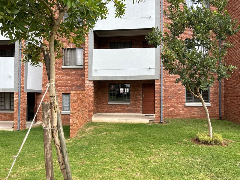 Rear view of a face brick apartment building featuring a ground floor tiled patio, landscaped garden area, and aluminium window frames.