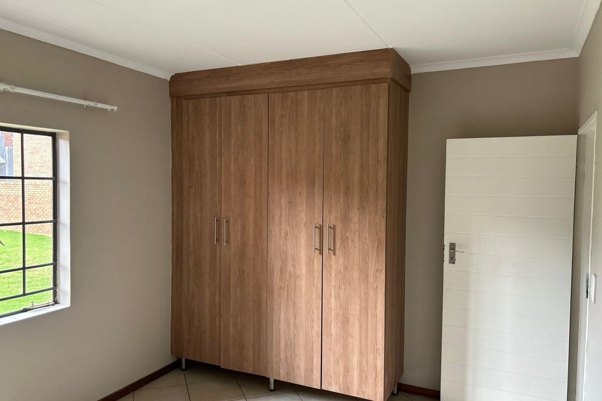 A clean, empty bedroom featuring neutral walls, tiled flooring, and a large built-in wooden wardrobe with ample storage space.