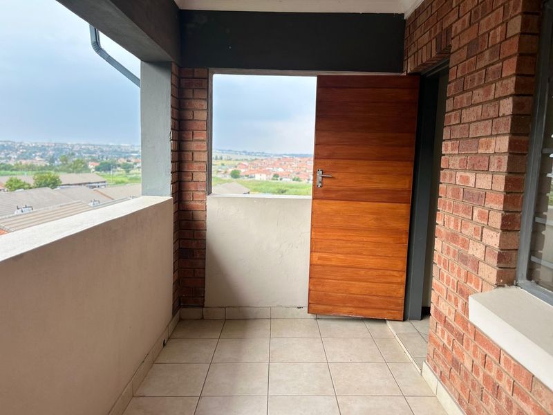 A covered balcony featuring exposed brick walls, tiled flooring, and a timber door, offering elevated views of the surrounding area.