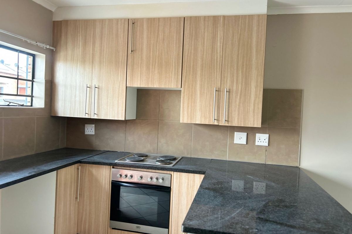 A functional kitchen featuring light wood-finish cabinetry, dark laminate countertops, a built-in oven and hob, and neutral tiled backsplash.