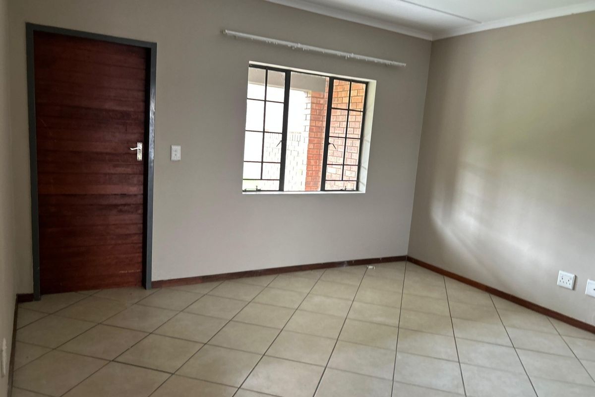 A clean, empty living room featuring neutral wall paint, tiled flooring, a timber door, and a steel-framed window.