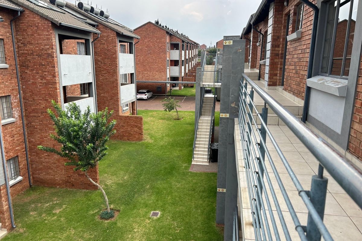 View of the apartment complex exterior featuring face brick buildings, communal garden space, external staircases, and elevated walkways with metal railings.
