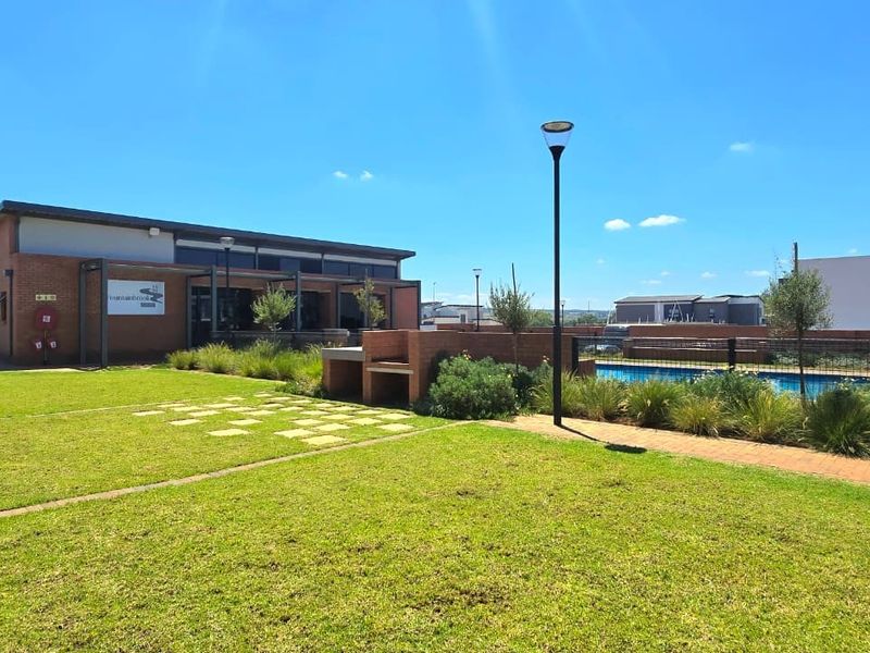 A well-maintained communal clubhouse area featuring a swimming pool, brick built-in braai, and landscaped garden space within a residential estate.