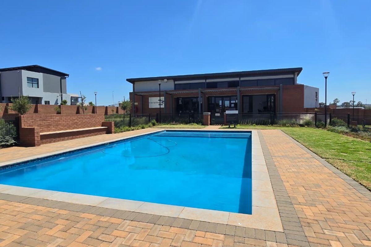 A well-maintained communal swimming pool area featuring brick paving, a built-in brick bench, and landscaped lawn, set against a modern brick building.
