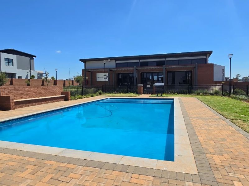 A well-maintained communal swimming pool area featuring brick paving, a built-in brick bench, and landscaped lawn, set against a modern brick building.