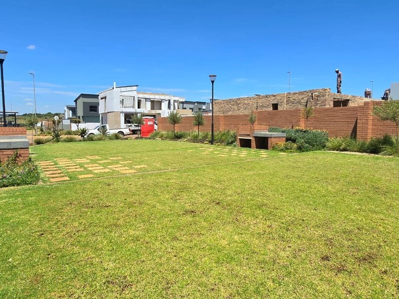 A well-maintained communal garden area featuring a manicured lawn, brick boundary wall, and a built-in braai facility.