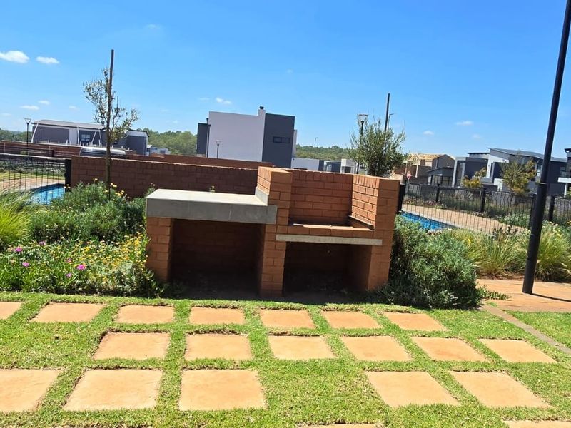 Outdoor entertainment area featuring a built-in brick braai with concrete countertop, set within a landscaped garden with paved patio space.