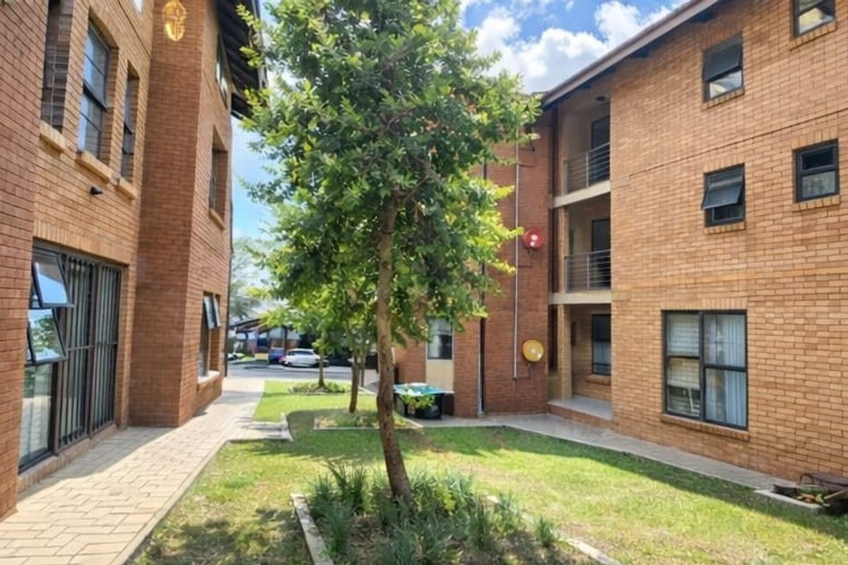 A view of the rear exterior of the apartment complex, featuring face brick facades, paved walkways, and a central garden area between the buildings.