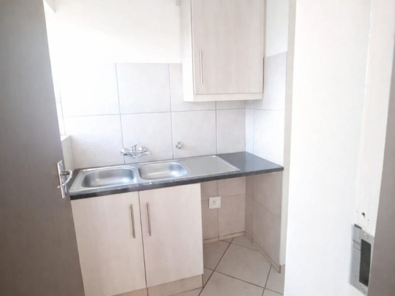 A compact scullery area featuring a double sink, laminate cabinetry, tiled splashback, and tiled flooring, providing a functional utility space.