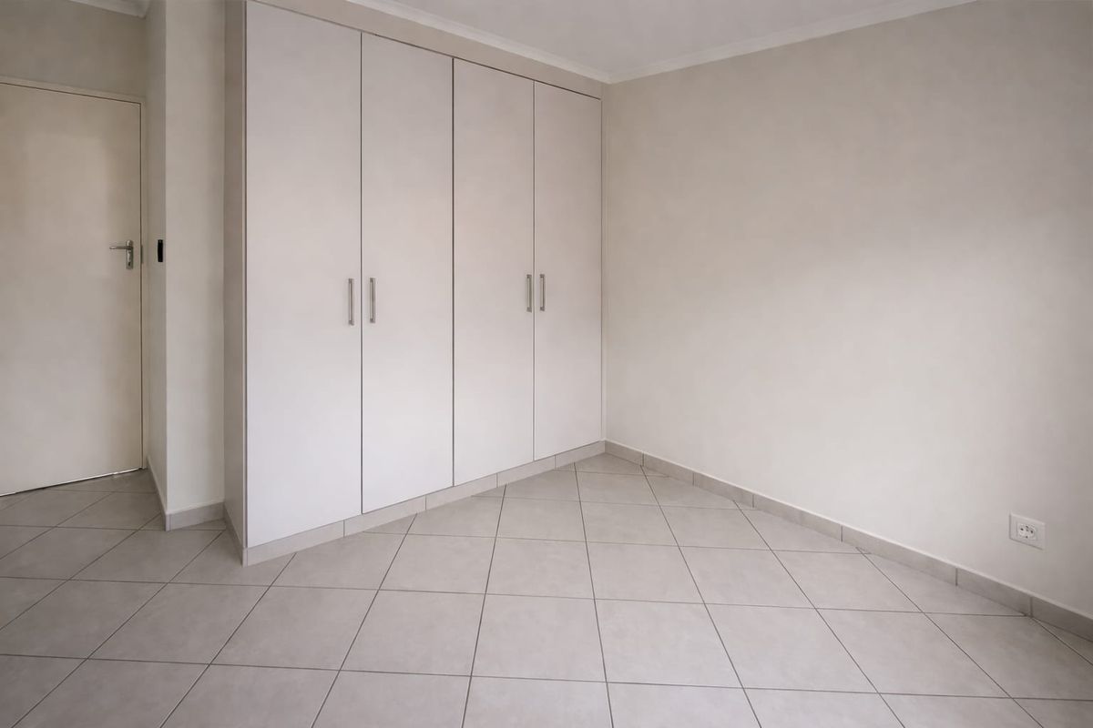 A clean, empty bedroom featuring neutral tiled flooring and ample built-in cupboard storage space.