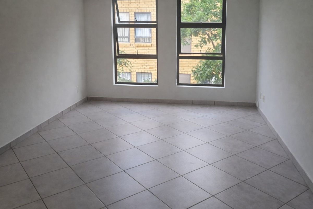 A bright, empty bedroom featuring neutral tiled flooring and large aluminium-framed windows, providing a clean and versatile space ready for personalization.