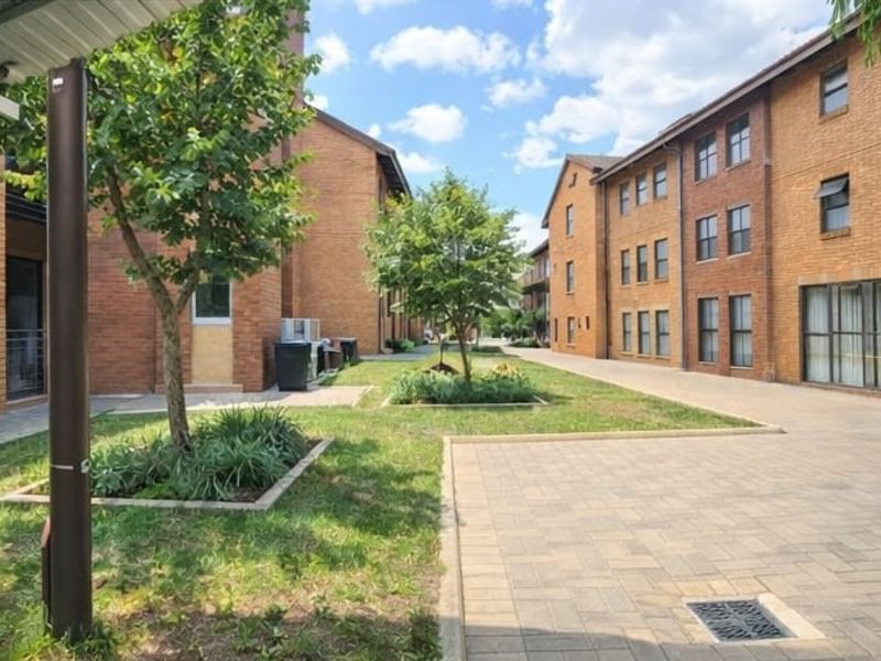 A view of the communal courtyard area between brick apartment buildings, featuring paved walkways and landscaped garden beds.