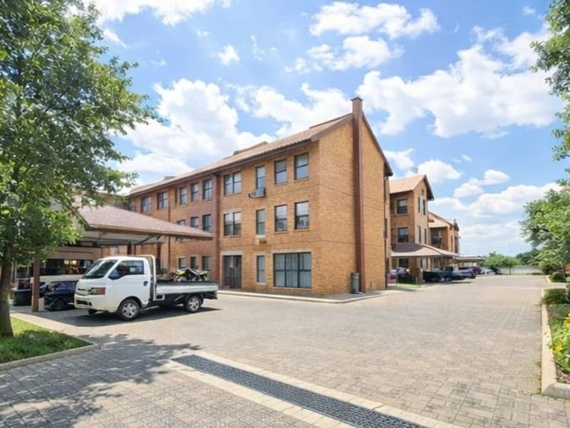Exterior view of a multi-story brick apartment complex featuring a paved driveway and covered parking areas.