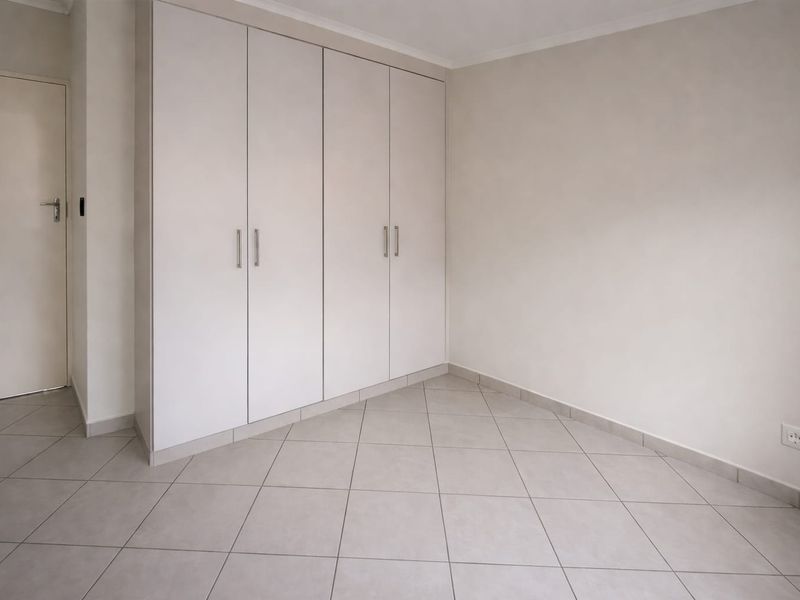 A clean, empty bedroom featuring neutral tiled flooring and ample built-in cupboard storage space.