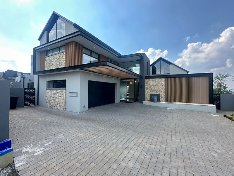 Modern architectural front elevation featuring stone and timber cladding, a paved driveway, double garage, and a striking entrance with a feature water wall.