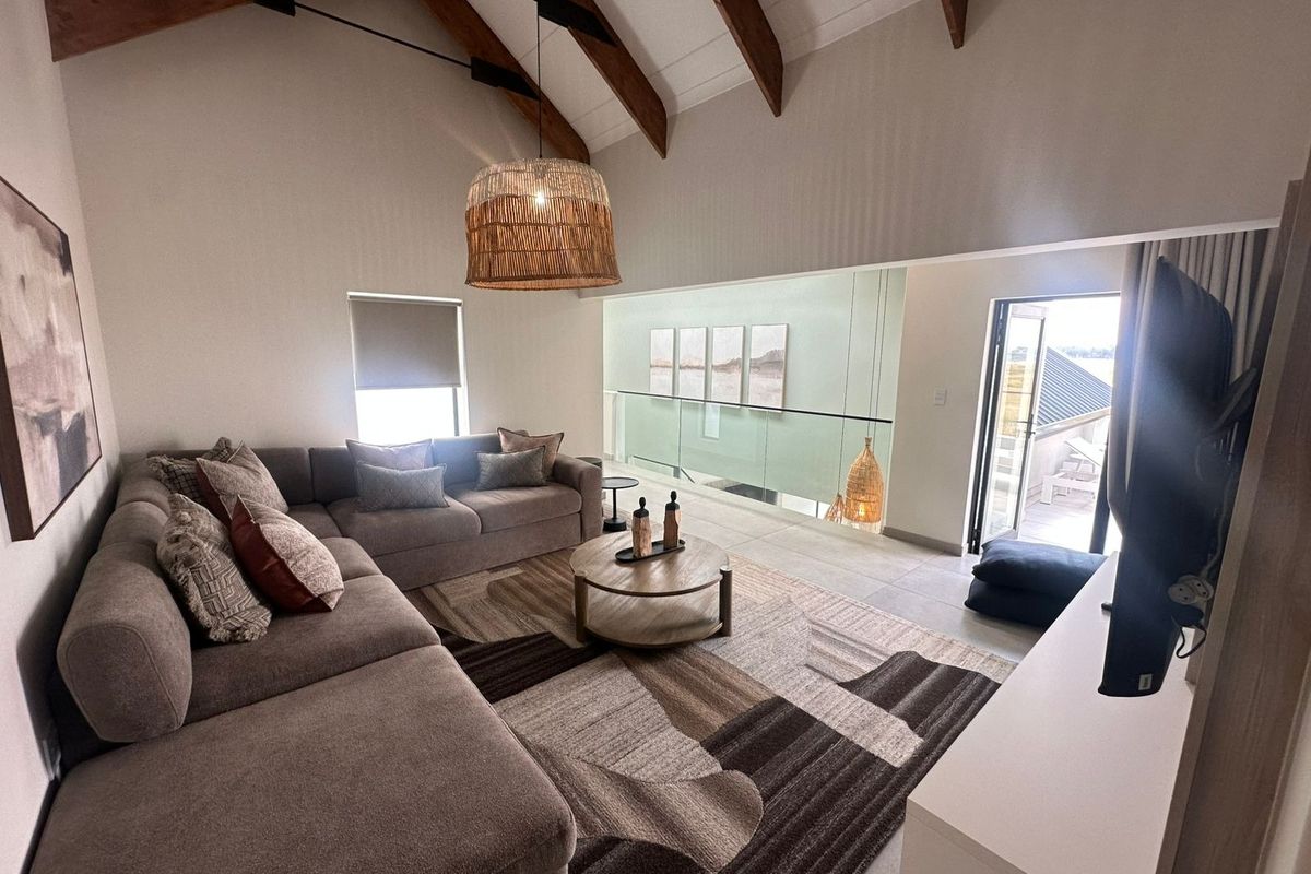 Spacious living area featuring a high vaulted ceiling with exposed timber rafters, tiled flooring, and a modern glass balustrade overlooking the lower level.