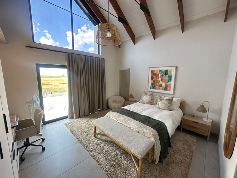 Spacious bedroom featuring a high vaulted ceiling with exposed timber beams, large windows, and direct access to an outdoor area through a sliding glass door.