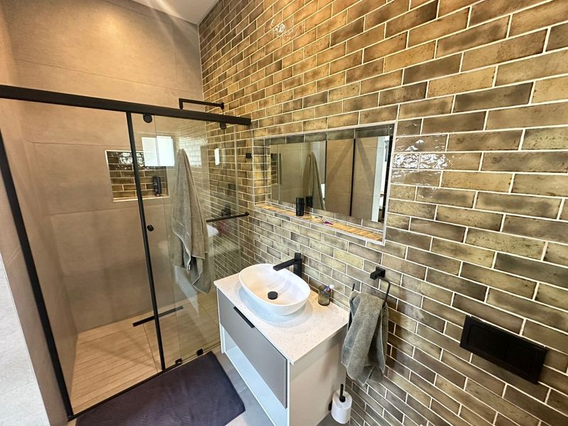 Modern bathroom featuring a glass-enclosed shower, a stylish vessel sink vanity, and a striking brick-style tiled feature wall with integrated mirror.
