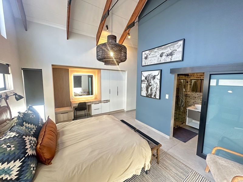 Spacious bedroom featuring high vaulted ceilings with exposed timber rafters, a modern built-in vanity, integrated wardrobe, and direct access to an en-suite bathroom.