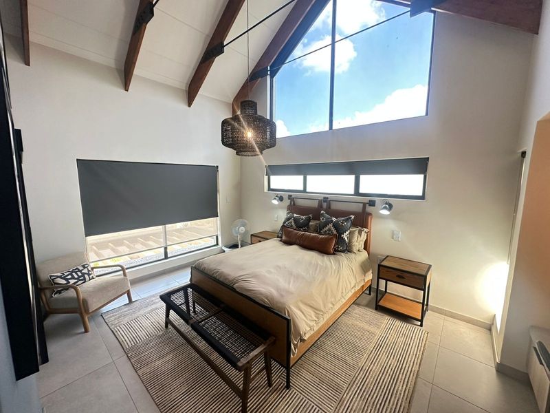 Spacious bedroom featuring a high vaulted ceiling with exposed timber beams, large feature windows, and modern tiled flooring.