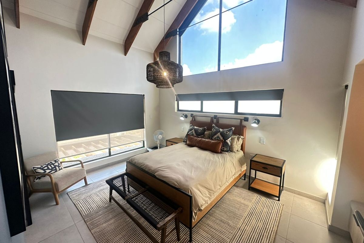 Spacious bedroom featuring a high vaulted ceiling with exposed timber beams, large feature windows, and modern tiled flooring.