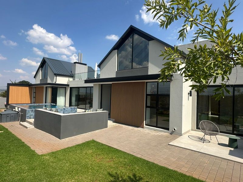 Modern rear exterior view featuring a paved patio, swimming pool, timber slat accents, and large glass windows under a contemporary pitched roof.