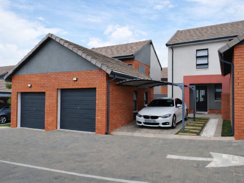 Front view of a modern townhouse featuring a double garage, a covered carport, and a paved driveway with a neat entrance area.