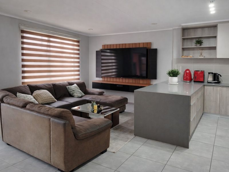 Modern open-plan living area featuring a sleek kitchen island, contemporary cabinetry, tiled flooring, and a dedicated wall-mounted media space.